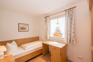 A small, single-room accommodation with a wooden bed, a desk, and a window with curtains. - Komfort-Ferienhaus Alpspitz (Grainau)