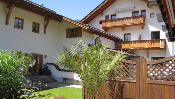 A traditional chalet with a wooden balcony, a garden with various plants, and a wooden gate. - Komfort-Ferienhaus Alpspitz (Grainau)