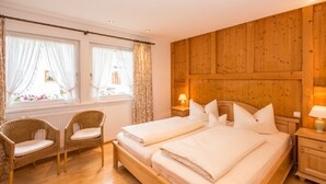 A bedroom with two beds, wicker chairs, a wooden headboard, and a window with curtains. - Komfort-Ferienhaus Alpspitz (Grainau)