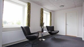 Una habitación con dos sillones negros, una mesita redonda y una puerta blanca.