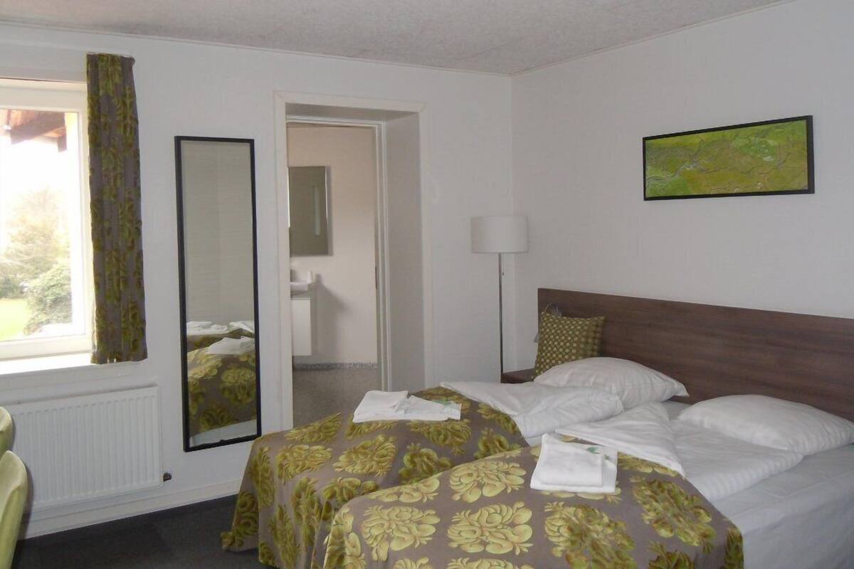 A hotel room with a bed, a mirror, a painting, and a window with curtains.