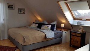 Et soveværelse med en seng, et natbord, en lampe, et lille skab og et vindue med udsigt til bygninger.