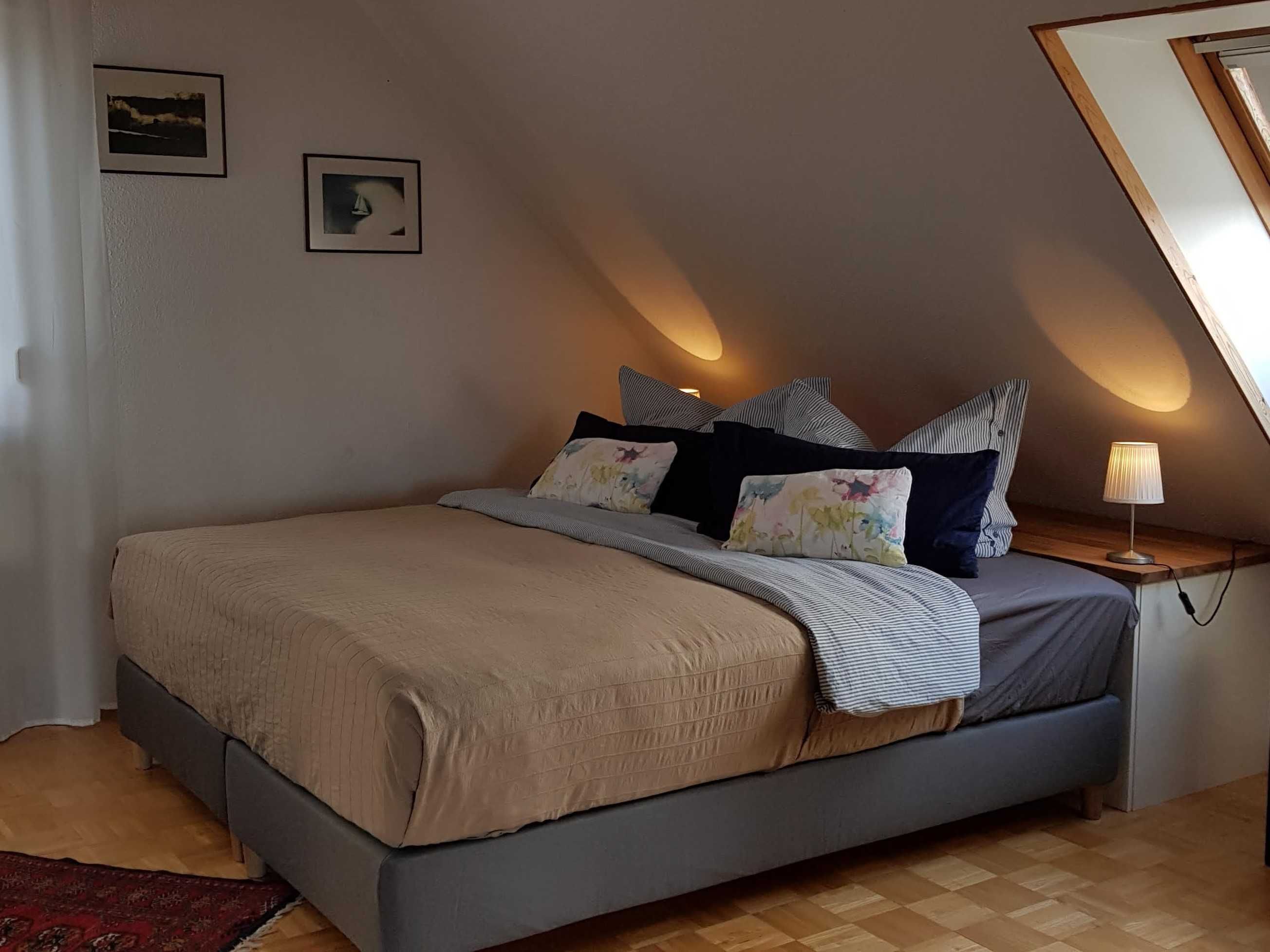 Une chambre à coucher avec un lit, des oreillers, une table de chevet et une lampe.