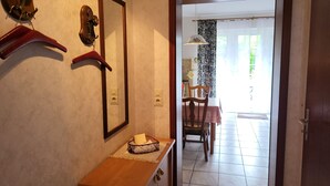 A hallway with a wooden bench, a mirror, and wall-mounted hooks. A dining area is visible through an open door.