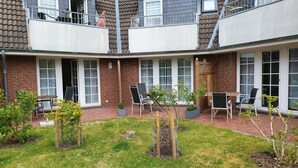 A residential building with a brick exterior, multiple windows, and a small garden area with outdoor seating.