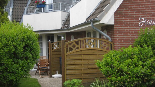 A two-story house with a balcony, a wooden gate, and a brick wall.