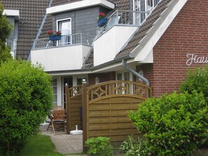 Une maison à deux étages avec un balcon, un portail en bois et un mur en briques.