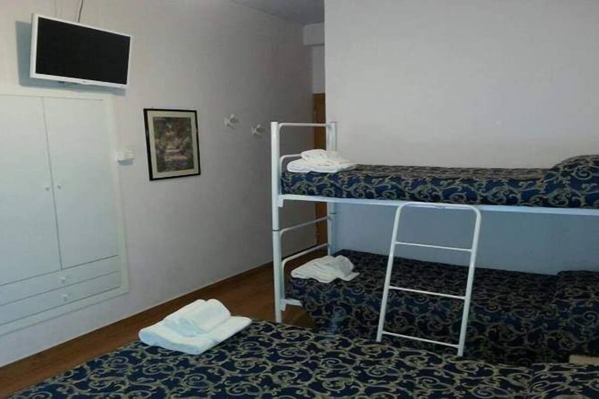 Una piccola stanza singola con un letto a castello, un armadio, una televisione e un quadro appeso al muro.