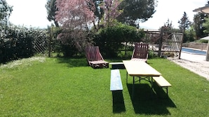 Un patio trasero con césped cuidado, dos sillas de madera y una mesa de picnic.