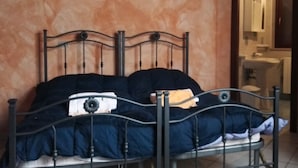Una cama con estructura metálica, un cuadro en la pared y un baño visible a través de una puerta abierta.