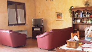 Un salón con techo de madera, un televisor sobre un mueble bajo, un sofá rojo, una mesita con objetos y una estantería con diversos artículos.