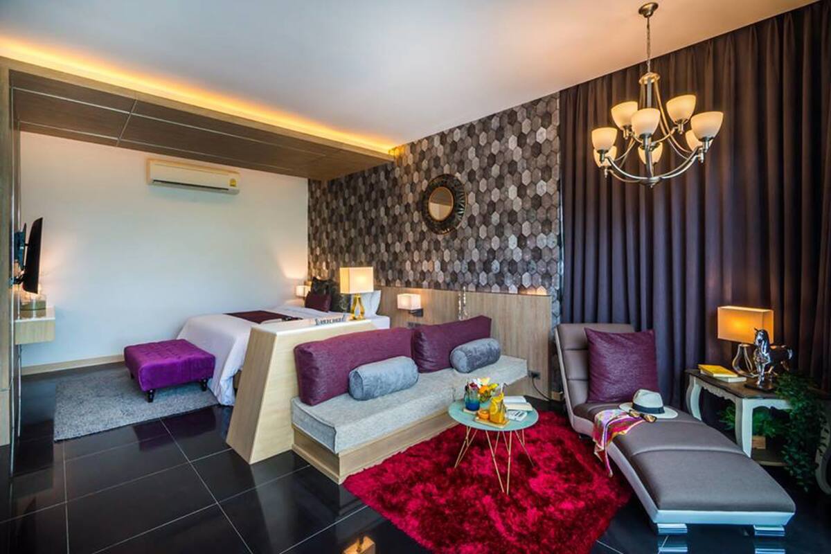A modern hotel room with a sofa, a chair, a small table, a red rug, and a chandelier.