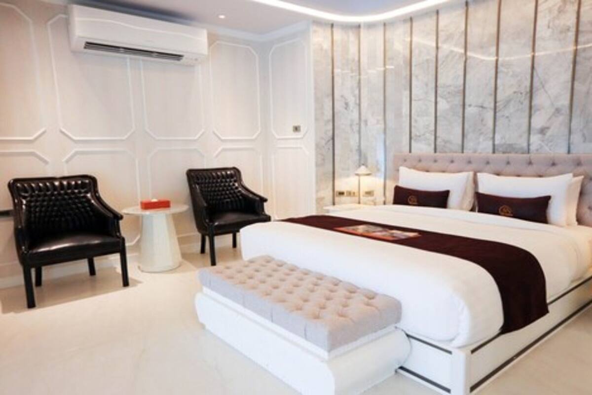 A modern bedroom with a large bed, two black chairs, a small round table, and a marble-patterned wall.