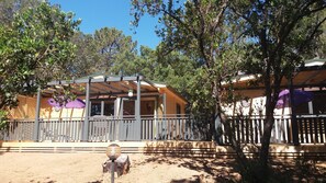 A wooden cabin with a covered porch, surrounded by trees and a fenced area. - village vacances KALLISTERRA (Zonza)