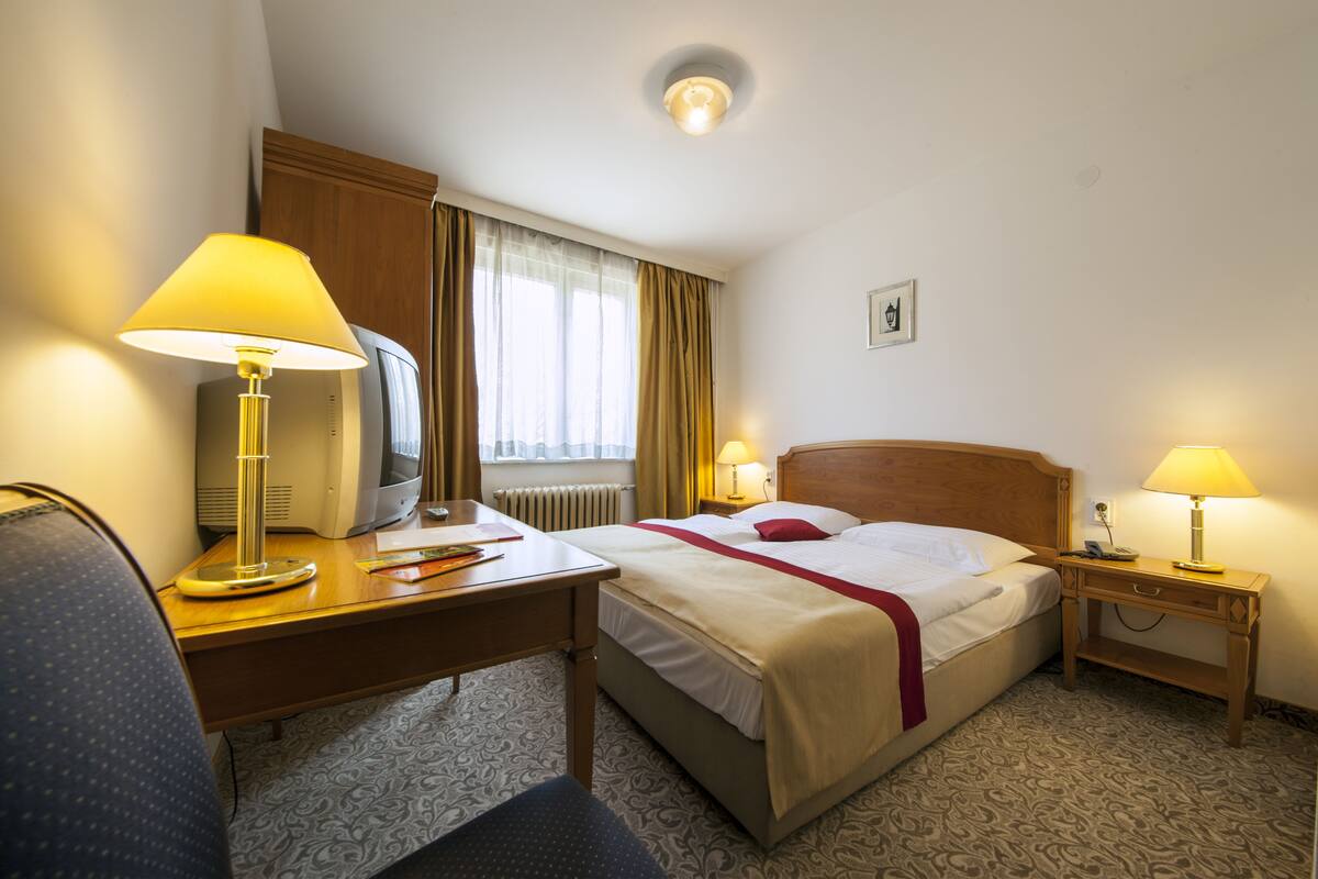 A hotel room with a bed, desk, and two bedside lamps.