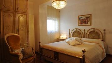 A bedroom with a large bed, a wooden chair, a chandelier, and a painting on the wall.