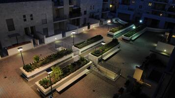 A courtyard with rectangular planters containing greenery, a paved walkway, and buildings with balconies and windows.