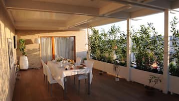 A dining area with a table set for four, surrounded by potted plants and a view of a cityscape.