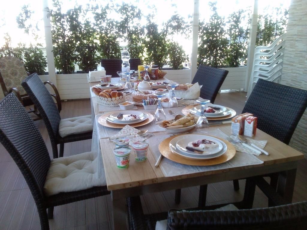 An outdoor dining area with wicker chairs, a wooden table set with various dishes, and a view of trees in the background.