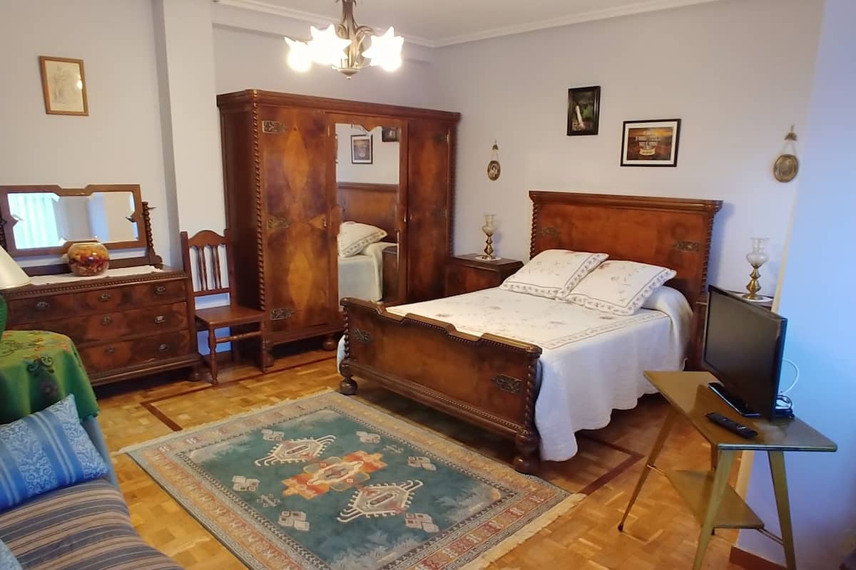 Une chambre à coucher avec un lit en bois, une commode, un miroir, une télévision et un tapis.