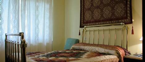 A bedroom with a bed, a radiator, a chair, and a wall hanging.