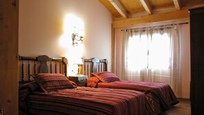 A room with two beds, wooden beams on the ceiling, a nightstand with a lamp, and a window with curtains. - La Casa de la Pradera (Carrizo)