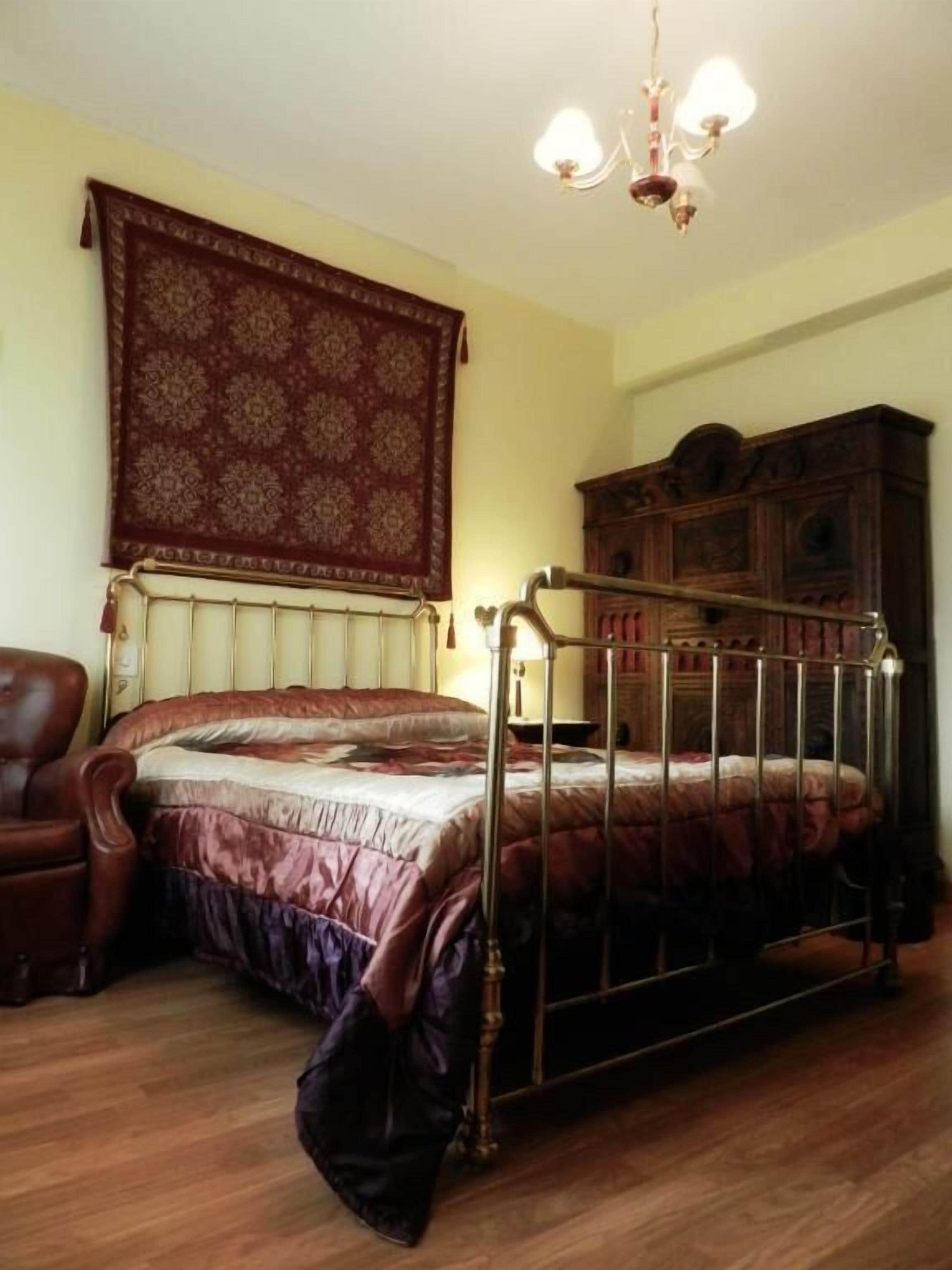 A bedroom with a bed, a wooden cabinet, a chair, and a patterned tapestry on the wall.