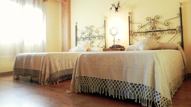 A room with two beds, wooden flooring, a wooden ceiling, and a window with curtains. - La Casa de la Pradera (Carrizo)