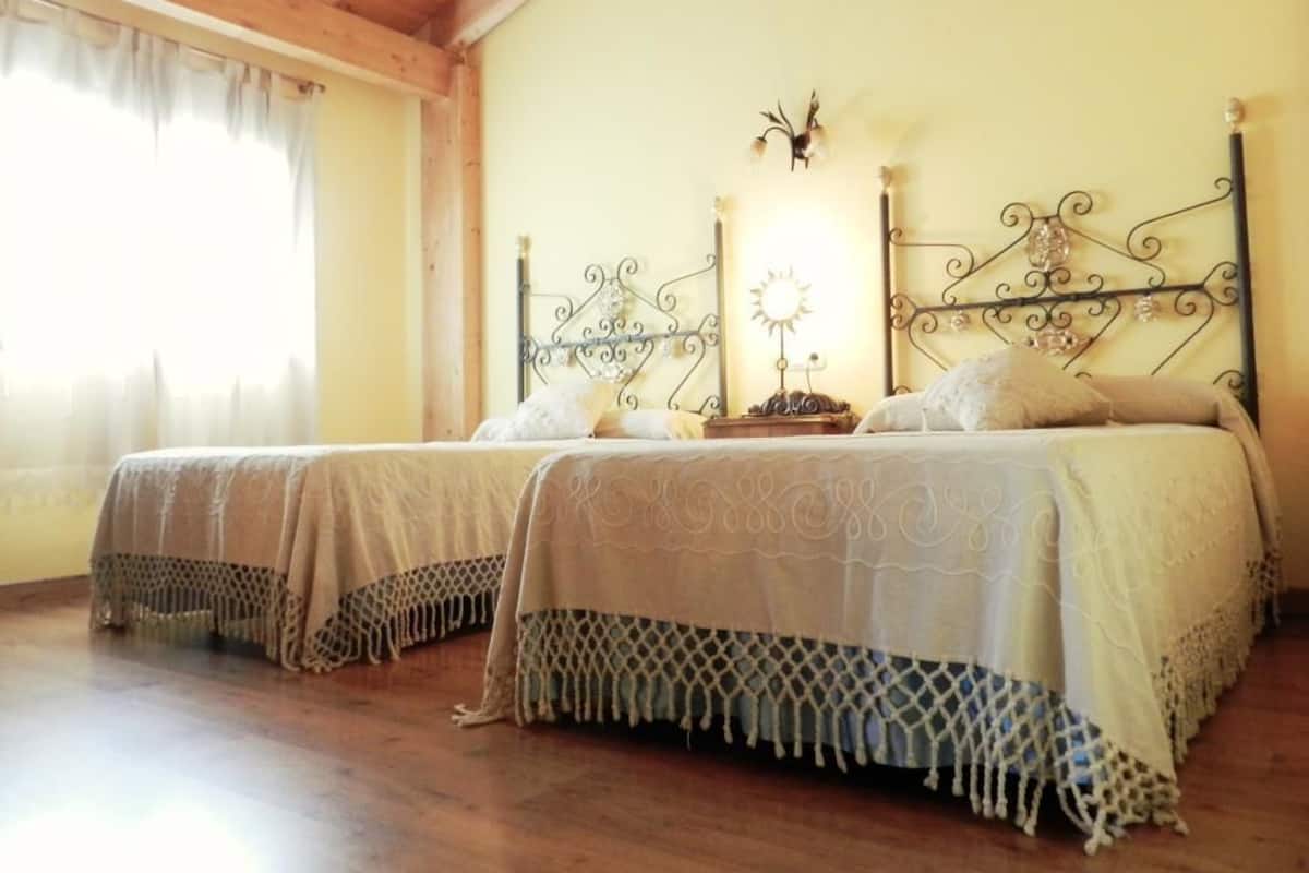 Une chambre avec deux lits, un plancher en bois, un plafond en bois et une fenêtre avec des rideaux.