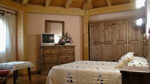 A bedroom with a wooden ceiling, a bed with a floral bedspread, a dresser with a television, and a large wooden wardrobe. - La Casa de la Pradera (Carrizo)