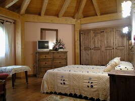 Un dormitorio con techo de madera, una cama con colcha estampada, un aparador con televisor y un armario grande de madera.