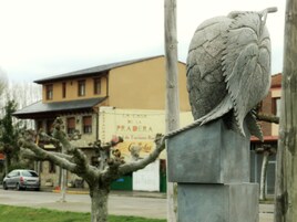 Una escultura de un búho sobre un pedestal, con un edificio al fondo.