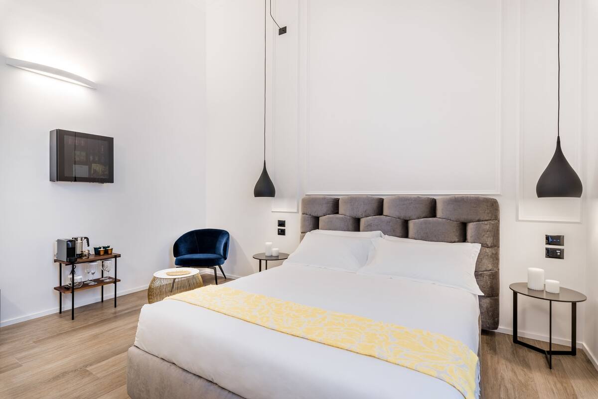 Una camera d'albergo moderna con un letto grande, un piccolo tavolino, una sedia e una mensola a parete.