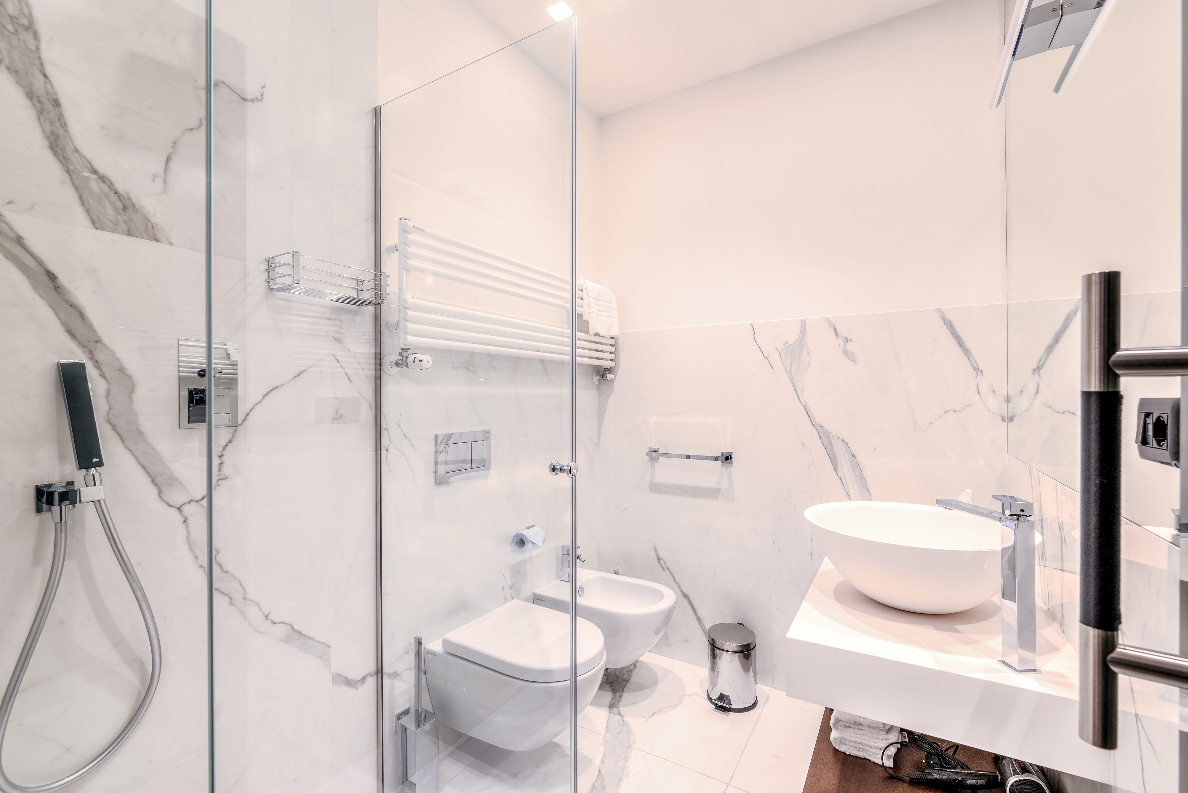 Un baño moderno con ducha de vidrio, lavamanos blanco y dos bidés.