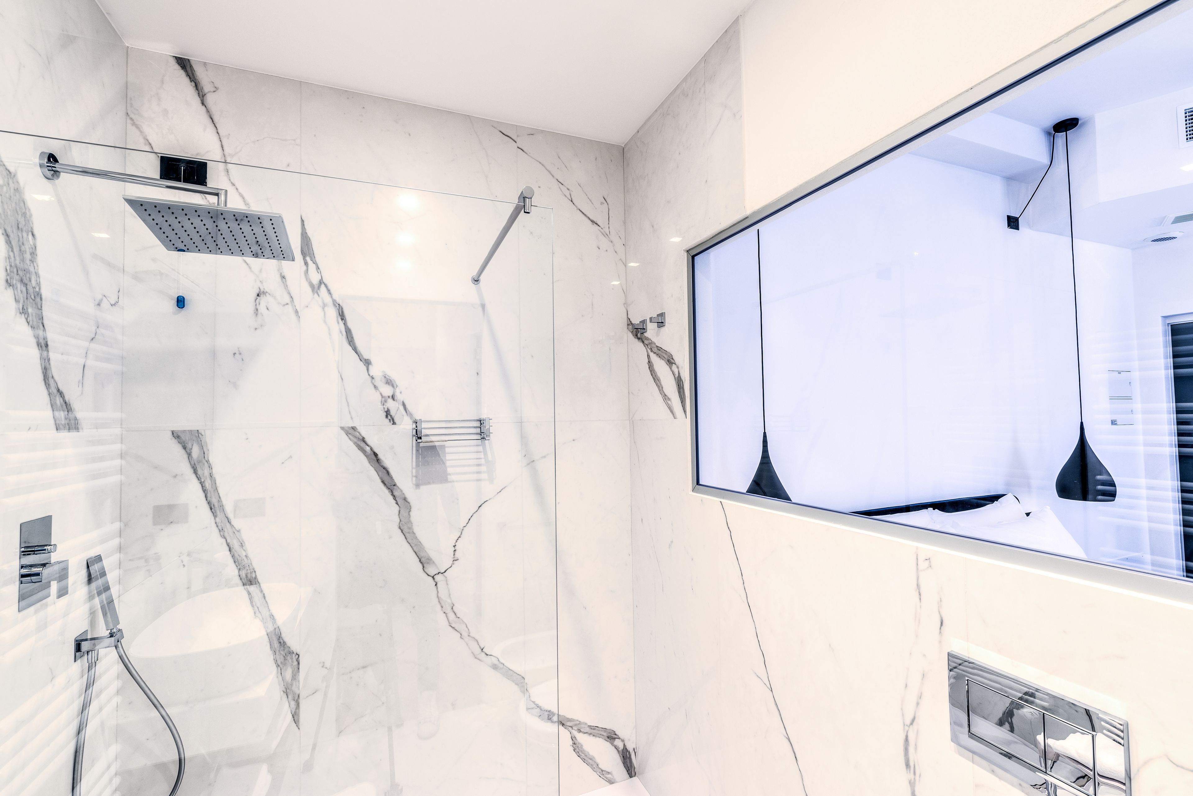 Un baño moderno con cabina de ducha de vidrio, paredes de mármol y un espejo grande.
