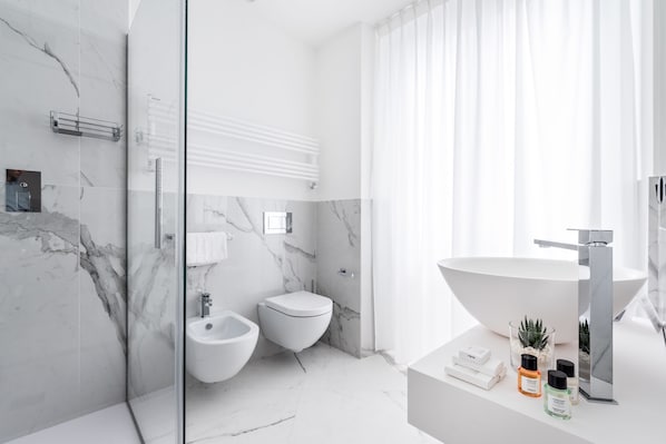 A modern bathroom with a large sink, bidet, and toilet, marble walls, and a glass shower enclosure. - La Spezia by The First (La Spezia)