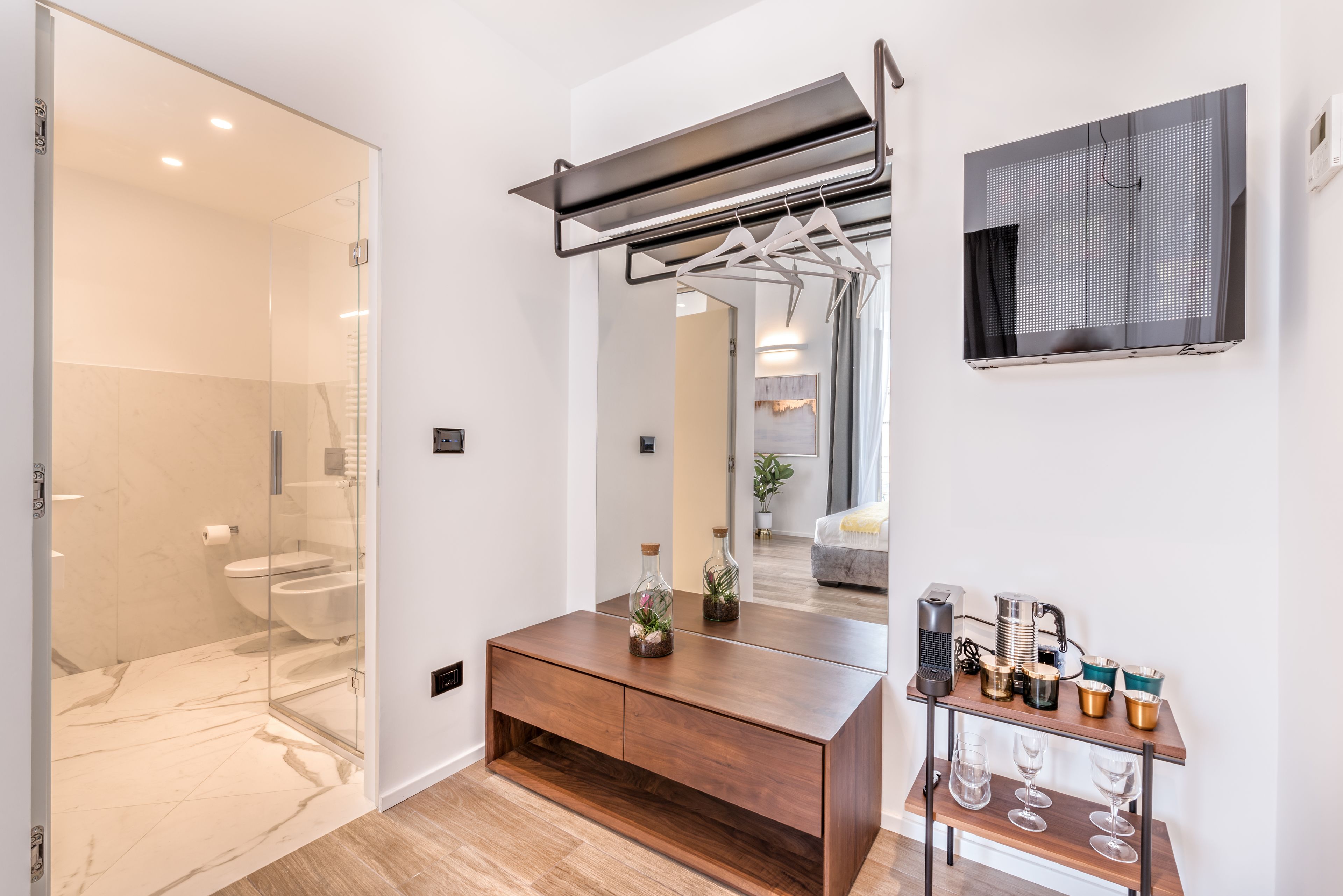 Un baño moderno con cabina de ducha de vidrio, tocador de madera con espejo y una pequeña mesita con cristalería.