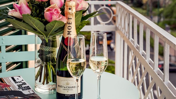 A table with a bottle of Moët & Chandon champagne, a glass of champagne, and a bouquet of pink flowers on a balcony.
