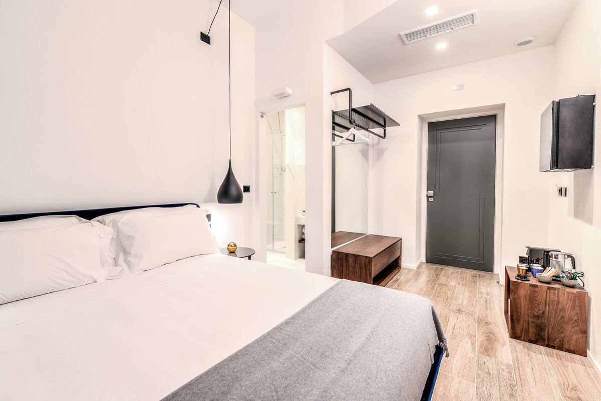 Camera d'albergo moderna con un letto grande, un tavolino in legno, uno specchio e una porta scura.