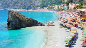 A beach with a rocky outcrop, clear turquoise water, and colorful umbrellas.