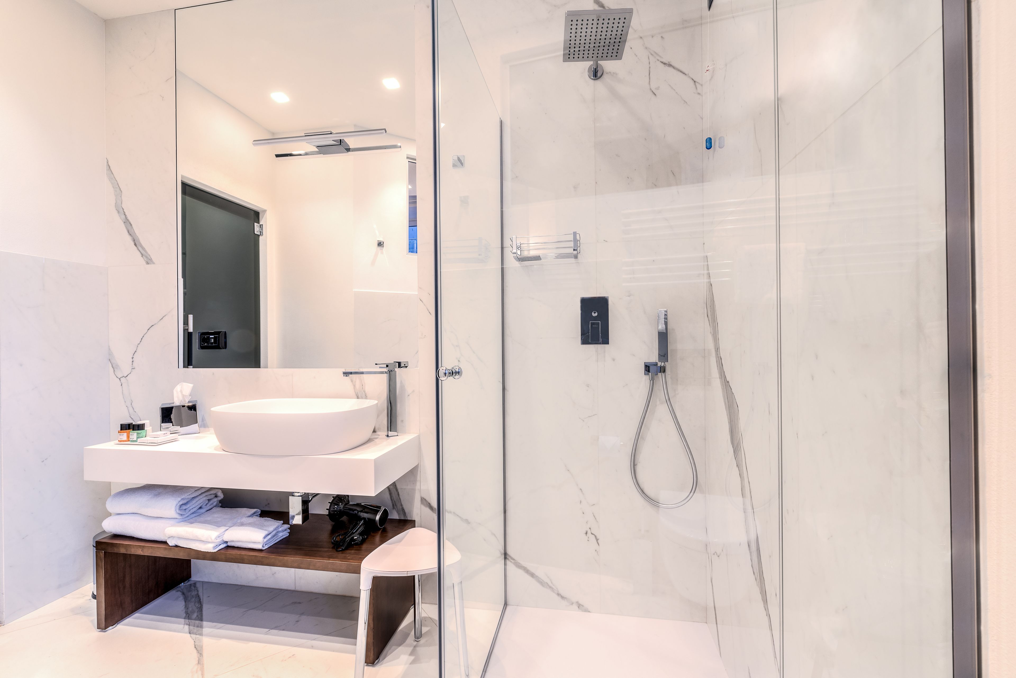 A modern bathroom with a glass-enclosed shower, a white sink, and a wooden shelf with towels.