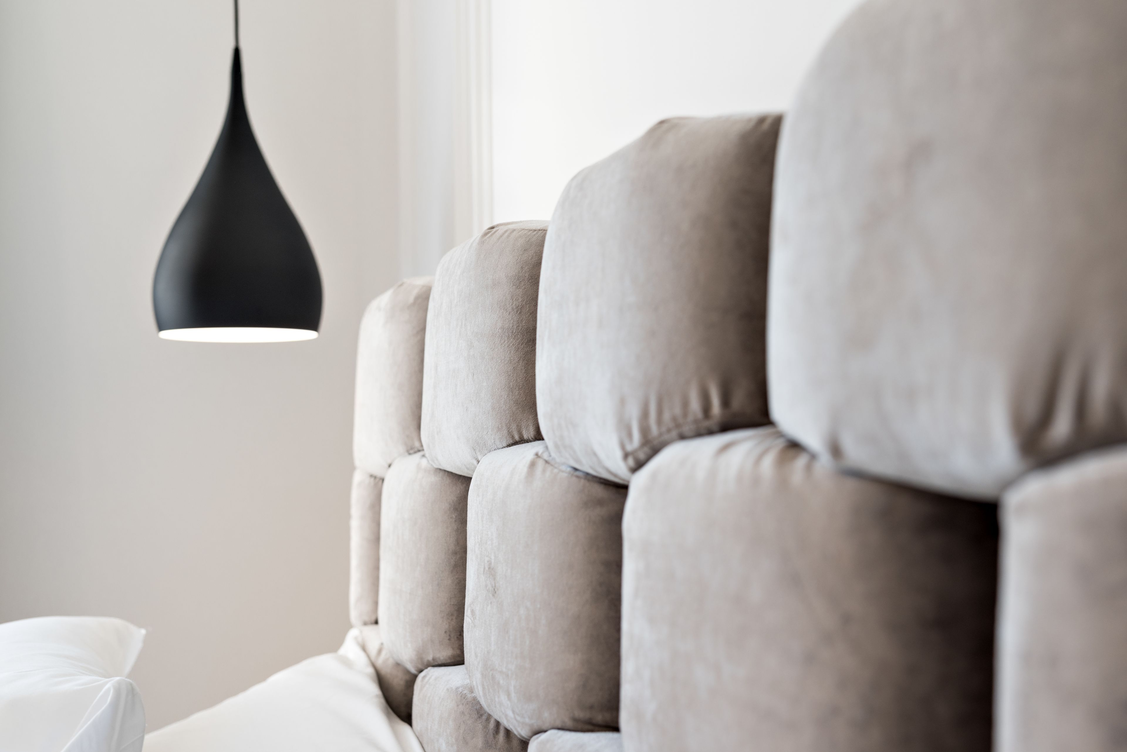 A close-up of a sofa with a tufted backrest and a black pendant light.
