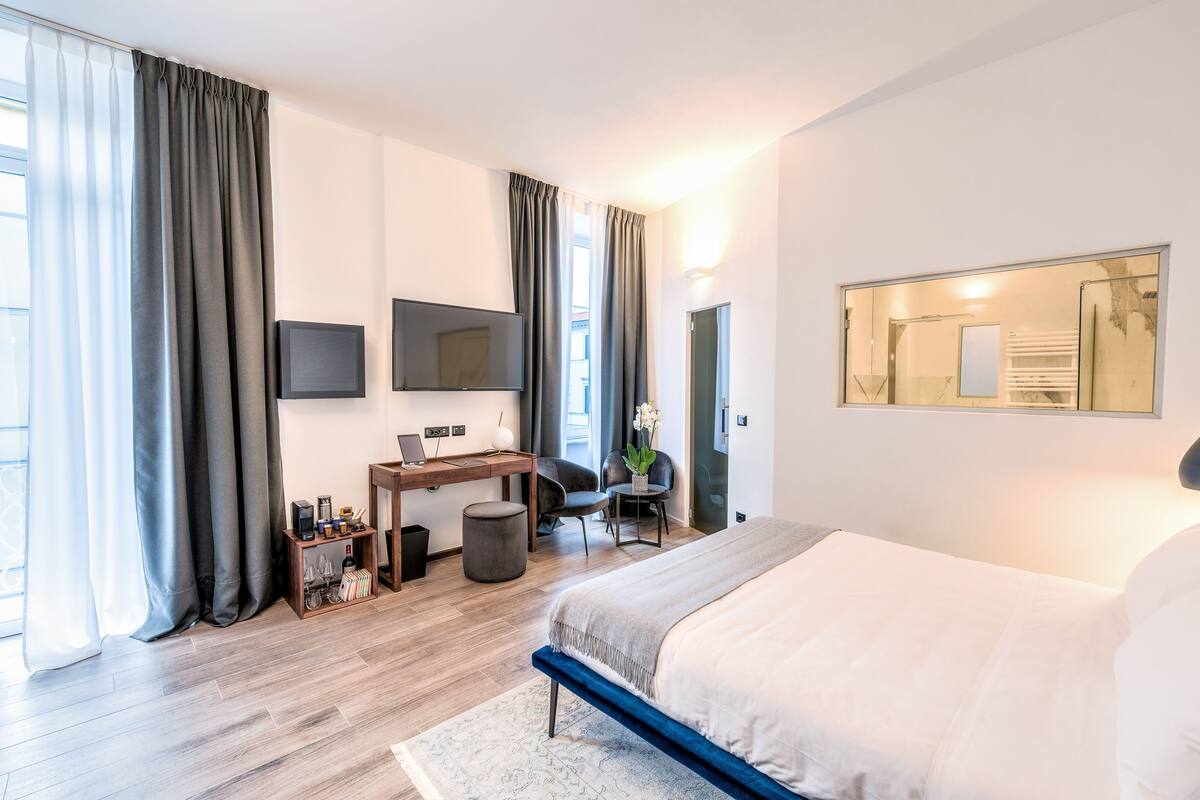 Una moderna camera d'albergo con un letto grande, una scrivania con un computer, una sedia e una TV a parete.
