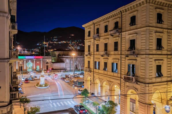 A nighttime cityscape with historic buildings, a roundabout, and a distant mountain range.
