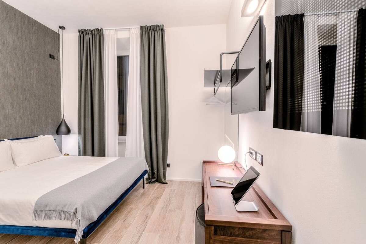 Una camera d'albergo moderna con un letto, un comodino, una lampada e uno specchio.