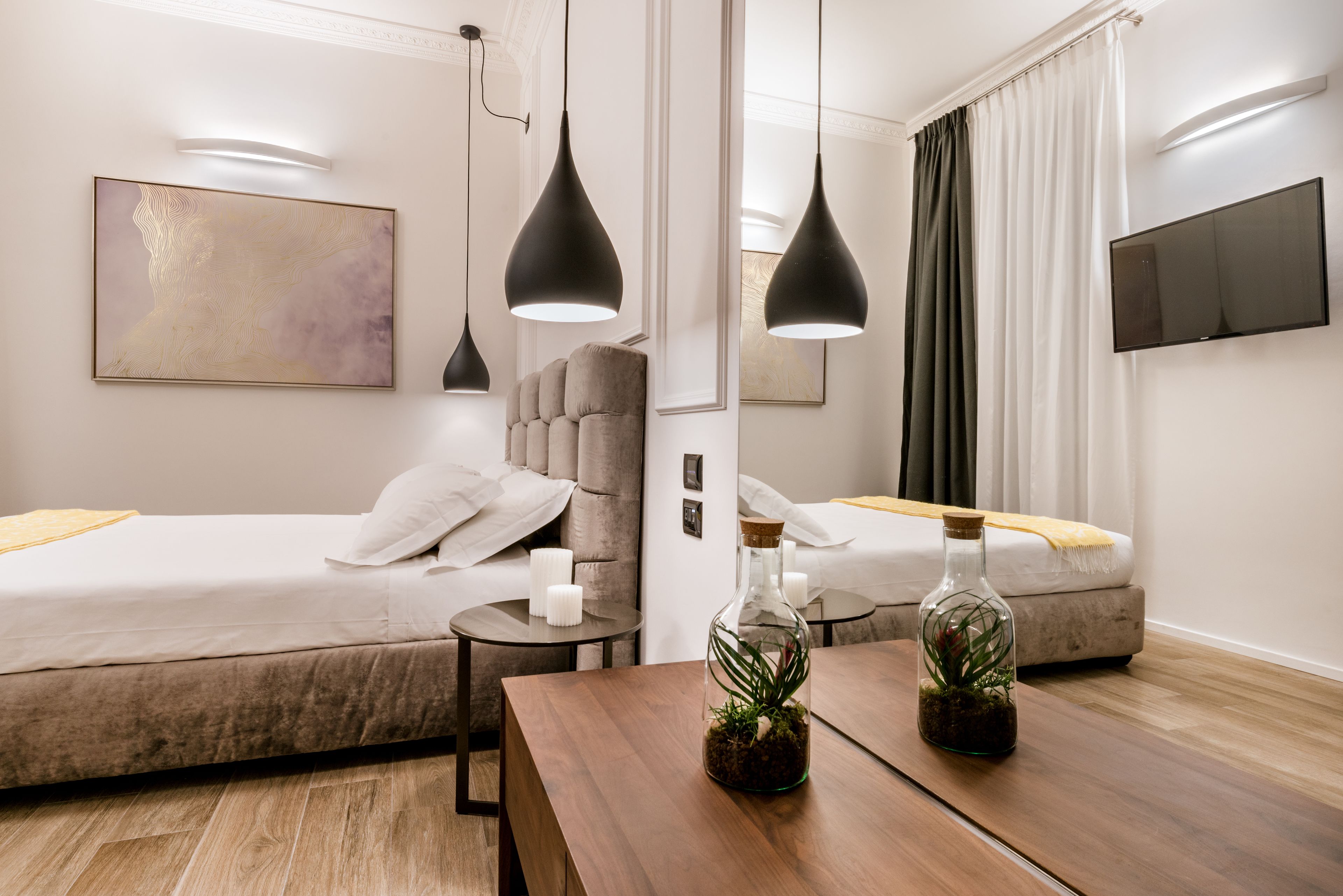 Una habitación de hotel moderna con dos camas, una mesa de madera, una mesita auxiliar pequeña, un televisor montado en la pared y un cuadro abstracto grande.