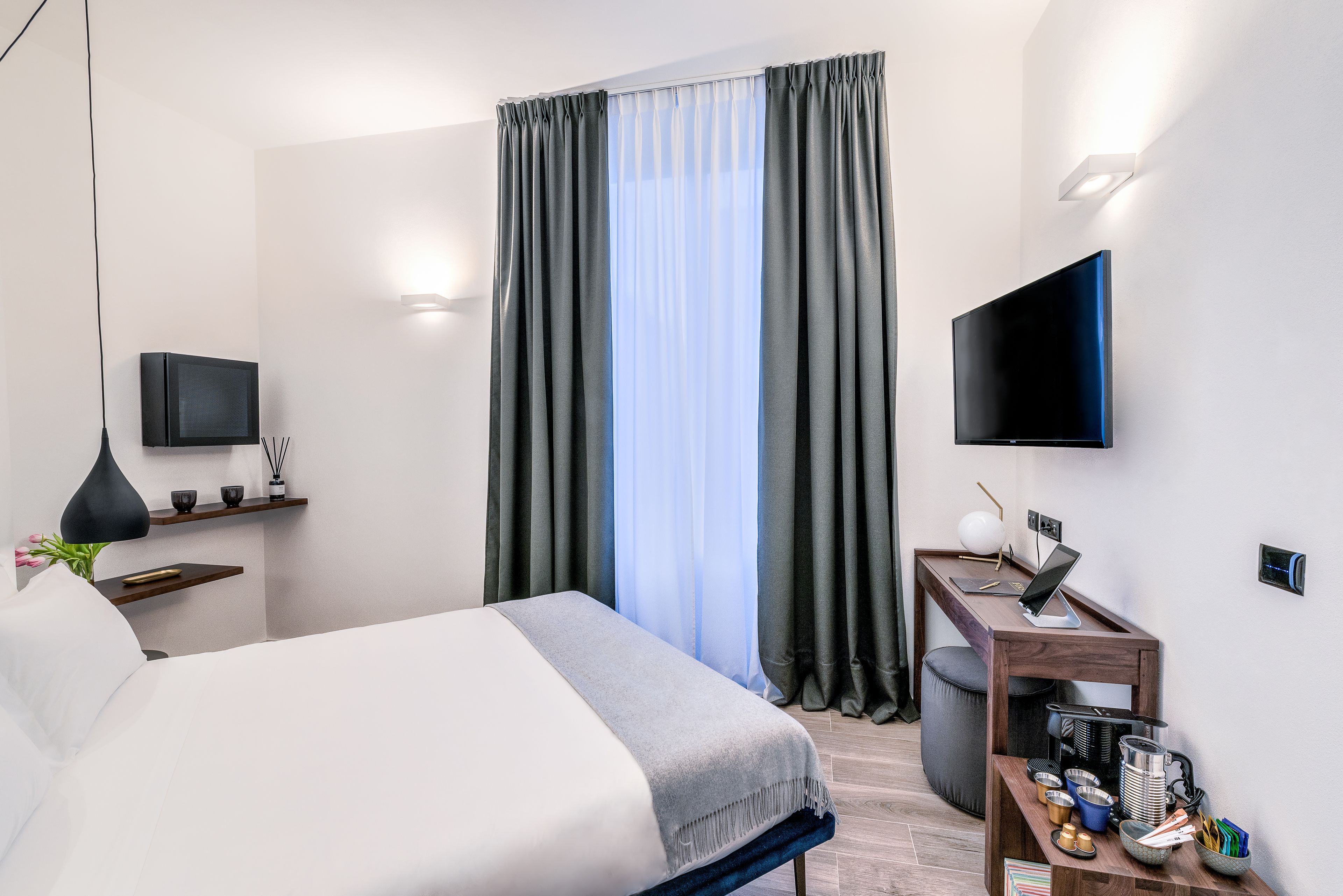 Ein modernes Hotelzimmer mit einem Bett, einem Schreibtisch mit einem Laptop, einem Fernseher und einem Fenster mit Vorhängen.
