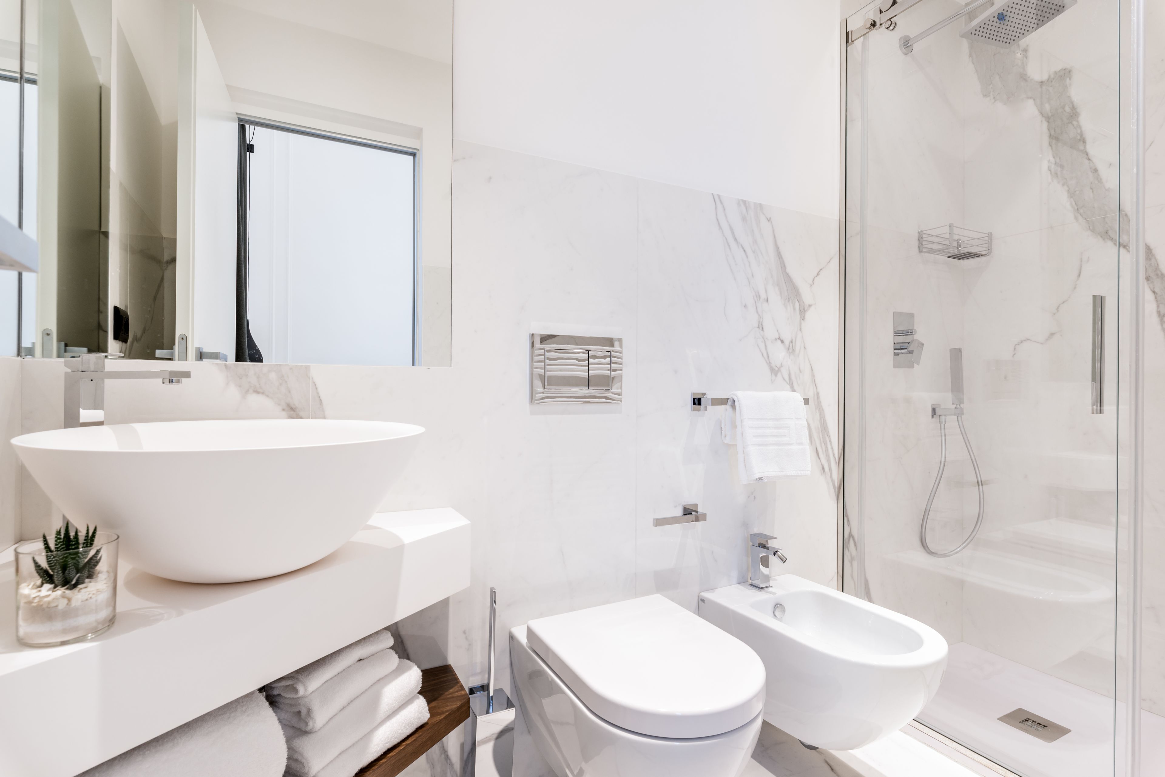 Une salle de bain moderne avec un grand lavabo blanc, des toilettes, un bidet et une douche à parois de verre.