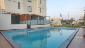 A rectangular swimming pool with a tiled edge, surrounded by a wooden deck. - Cygnett Lite (Alwar)