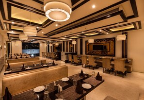 A hotel dining area with multiple tables and booths, a bar, and a large flat-screen TV mounted on the wall. - Cygnett Lite (Alwar)